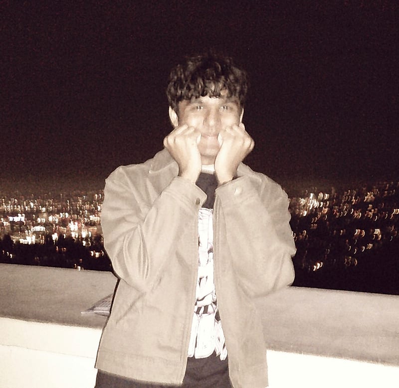 Aansh Singh resting his chin on his hands, with city lights behind him.
